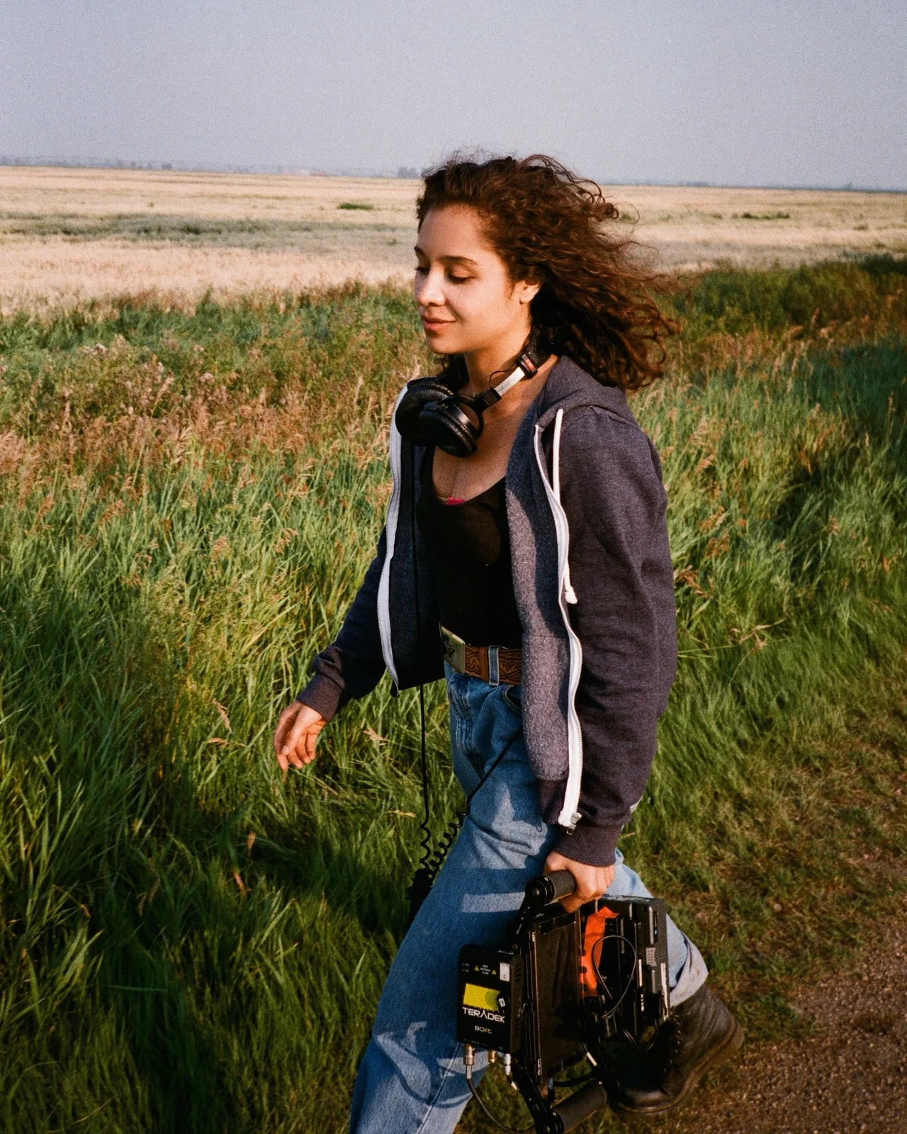 A filmmaker holding a camera in tall grass.