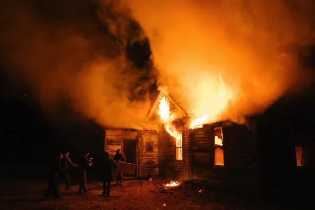 A wooden house burning at night.