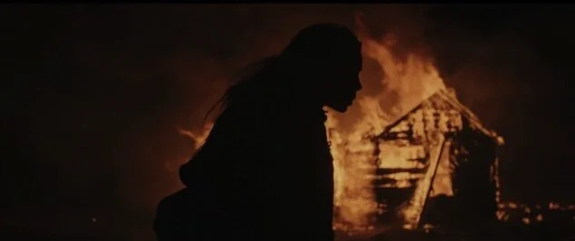 A woman’s silhouette in front of a burning house.
