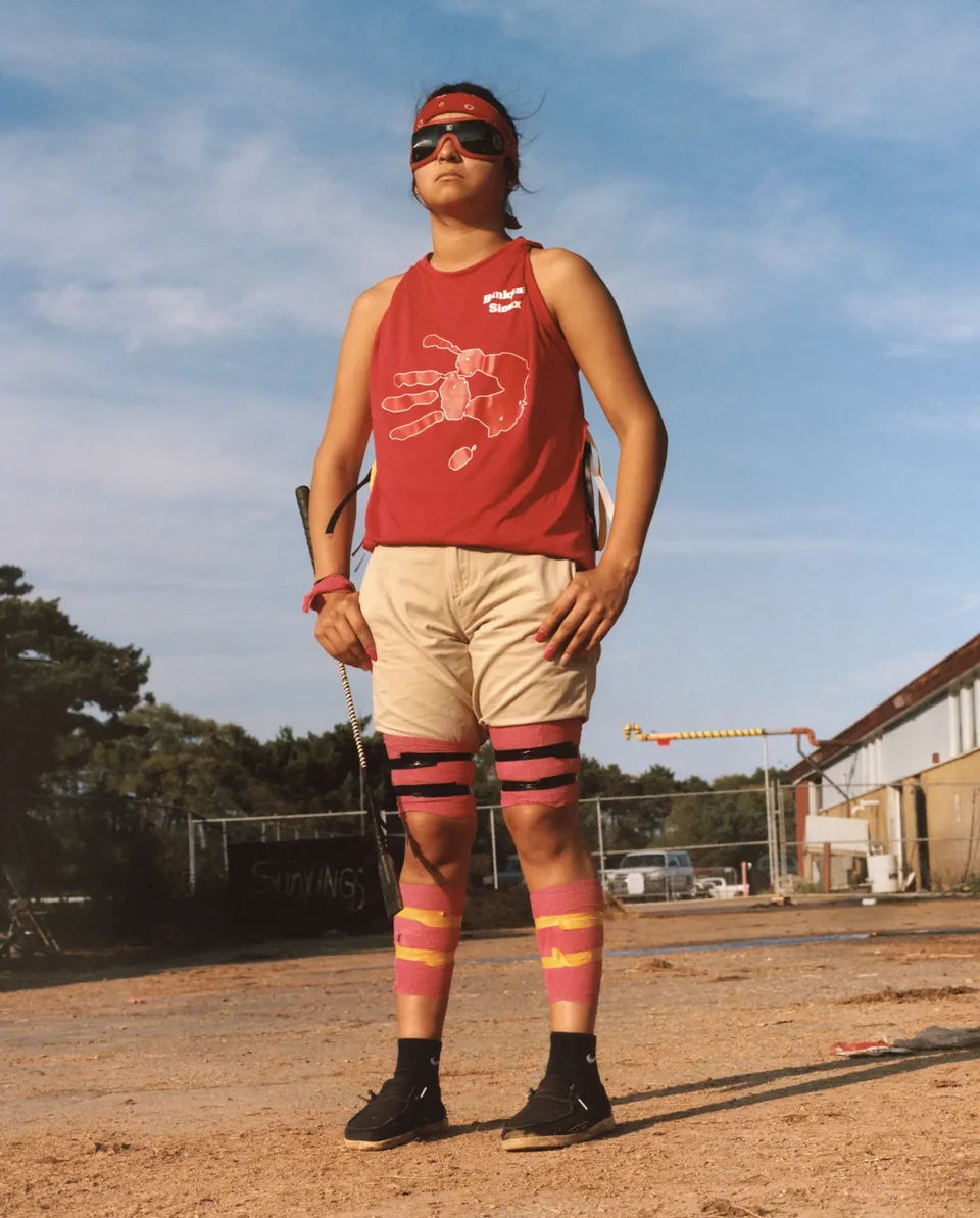A relay rider in a red sleeveless shirt and striped socks stands beneath a blue sky.