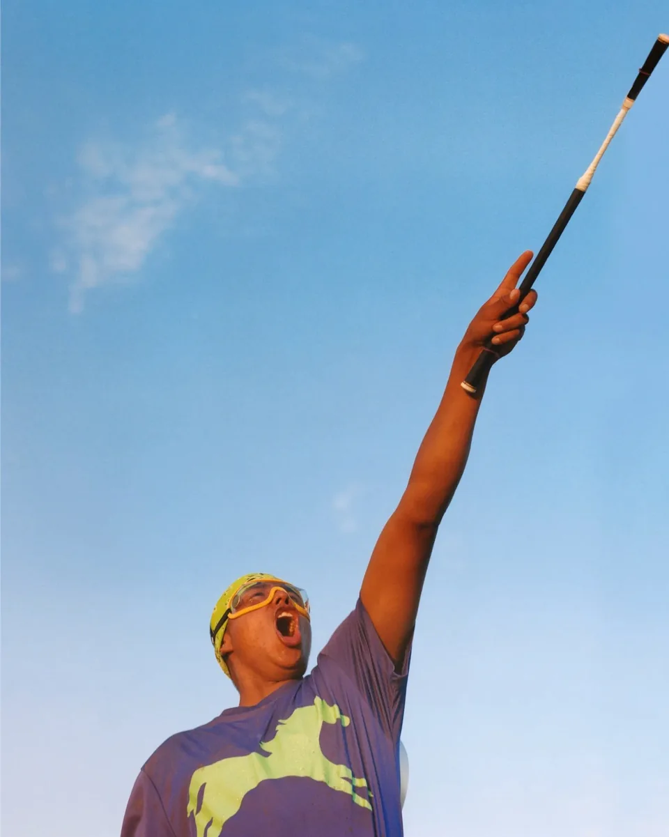 A relay team member raises an arm and riding crop against a clear blue sky.