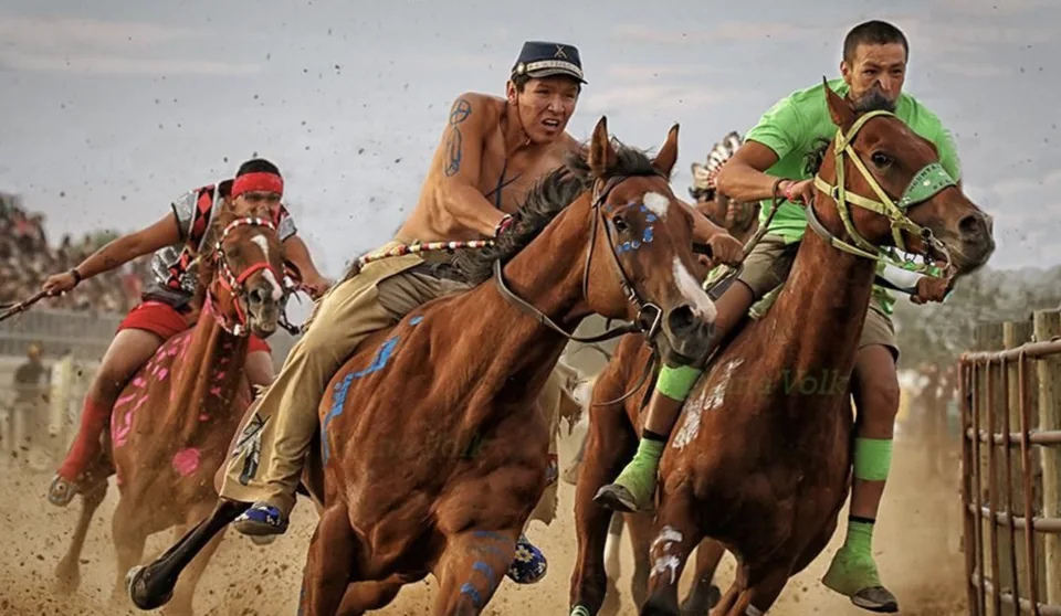 Three bareback riders lean forward as their horses race side by side.