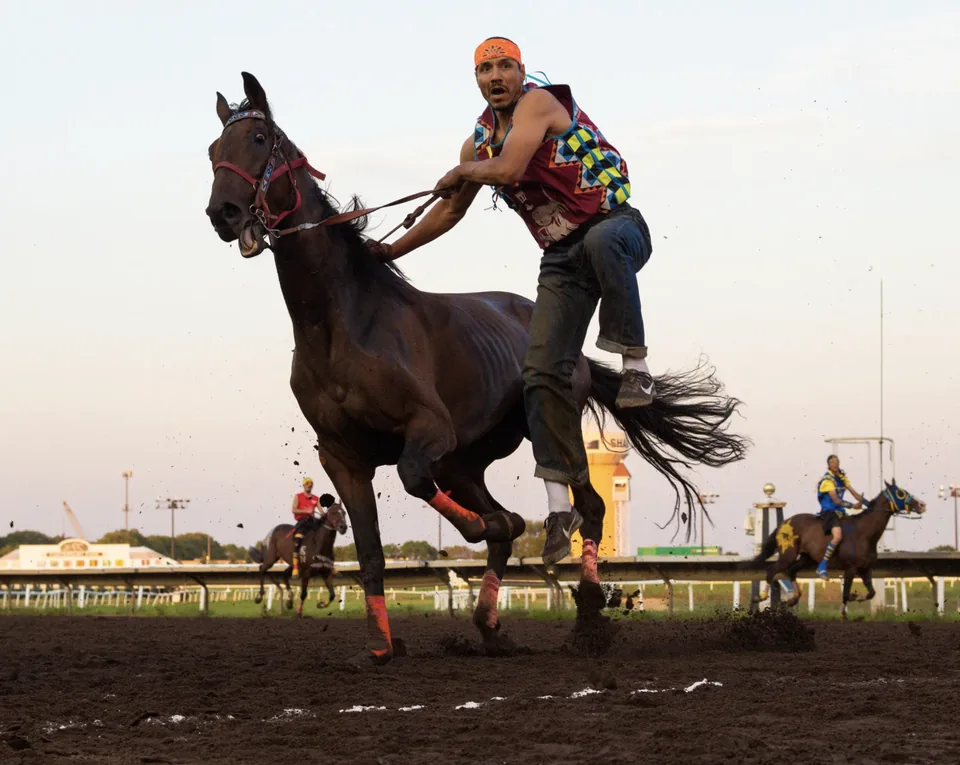 A relay rider springs onto a horse in mid-stride.