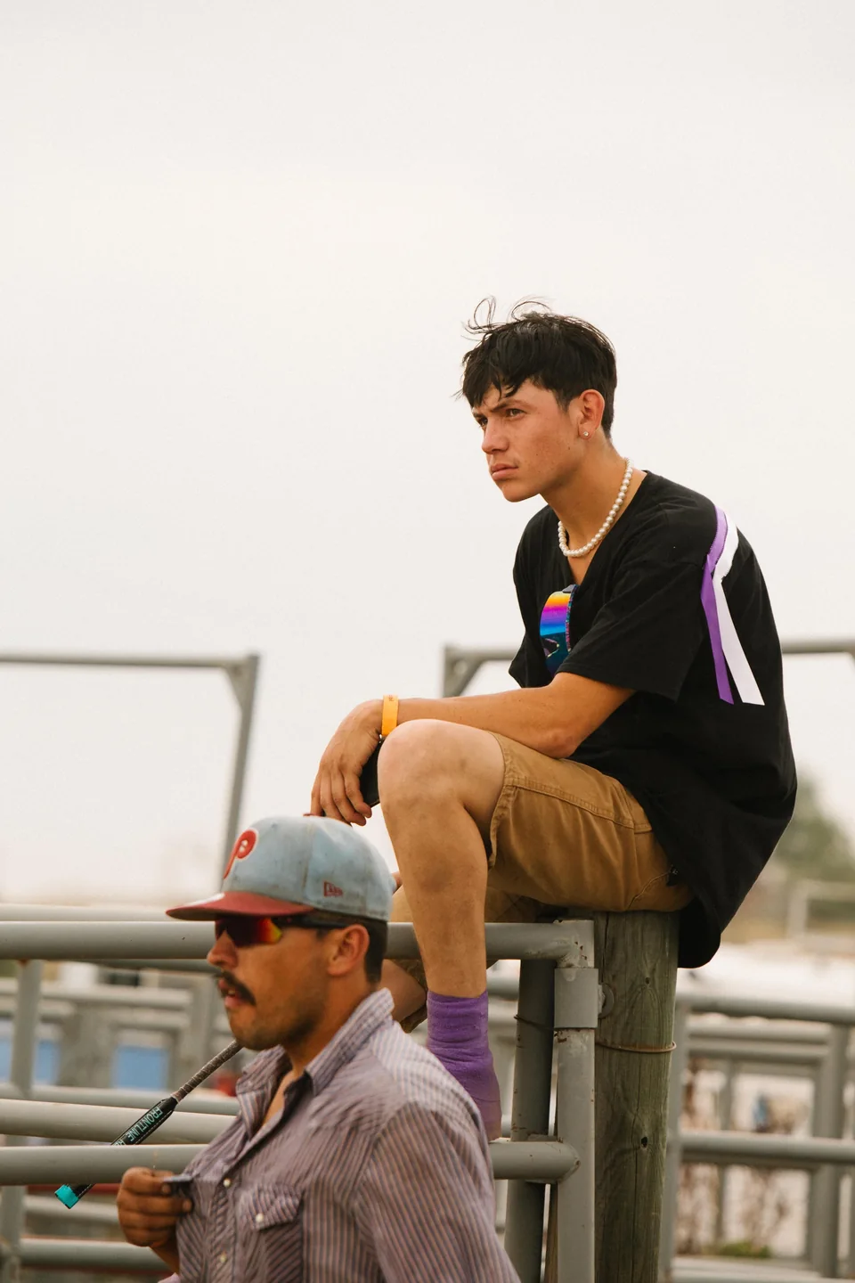 Two spectators watch from beside and on top of the track fence.