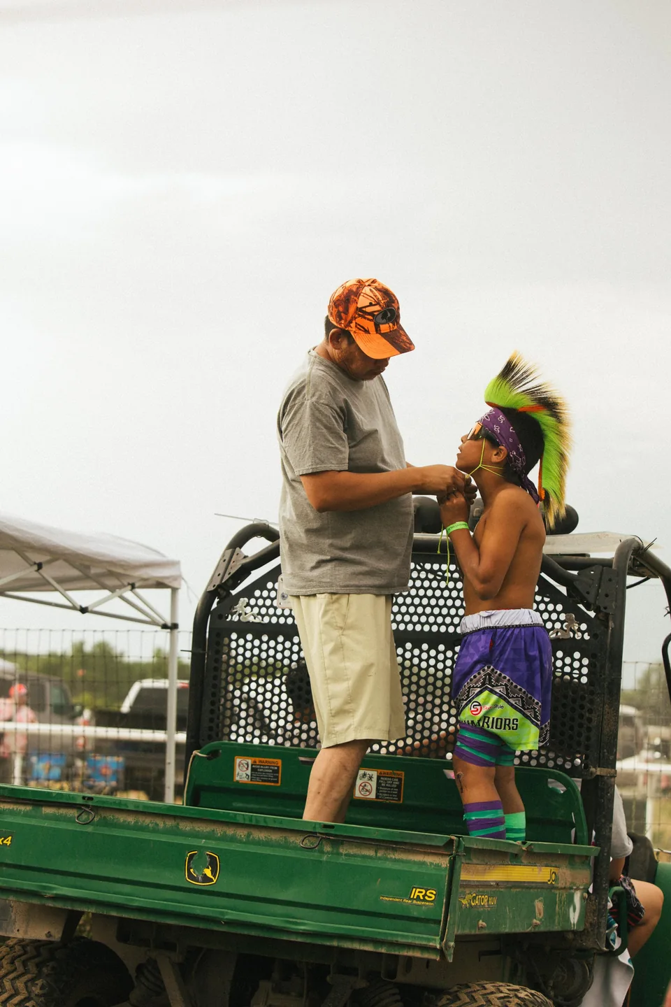 Two people stand on a green utility vehicle beside the track.