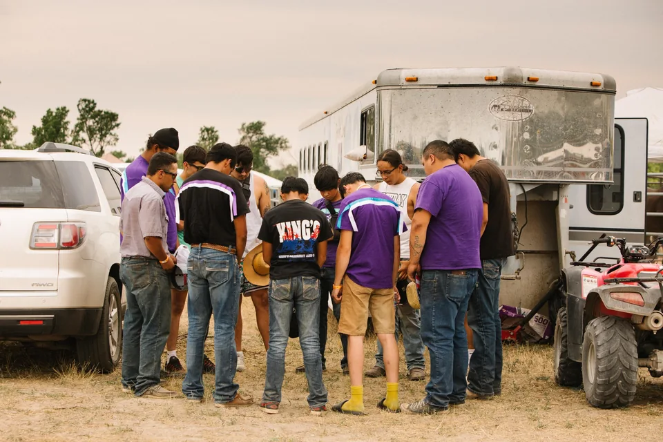 A relay team gathers in a circle beside a pickup and livestock trailer.