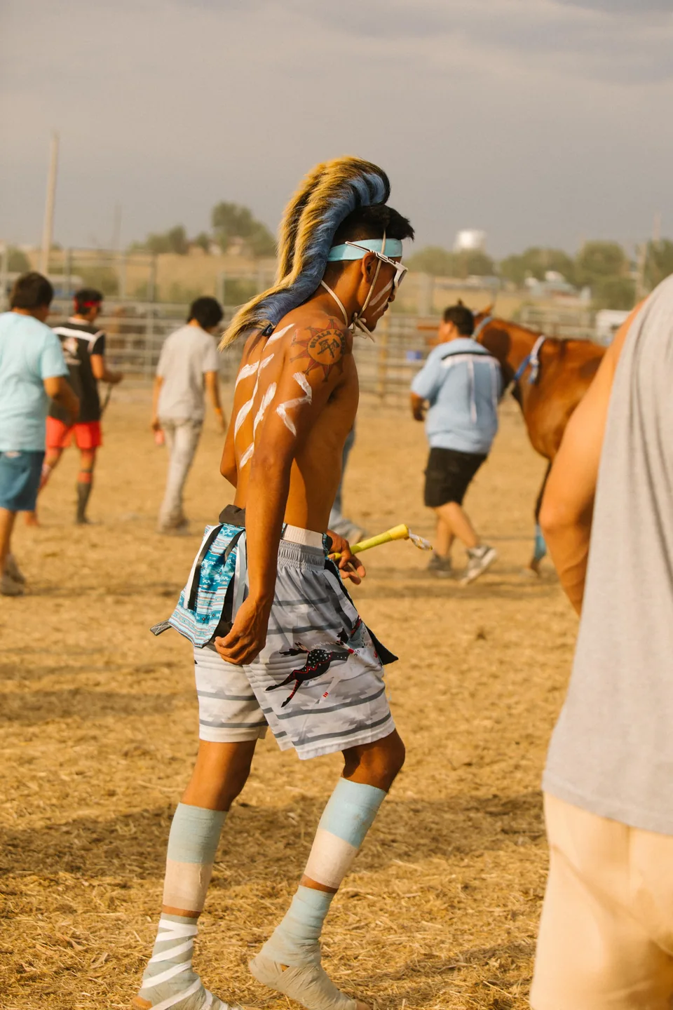 A rider with a blue head covering and pale leg wraps walks across the grounds.