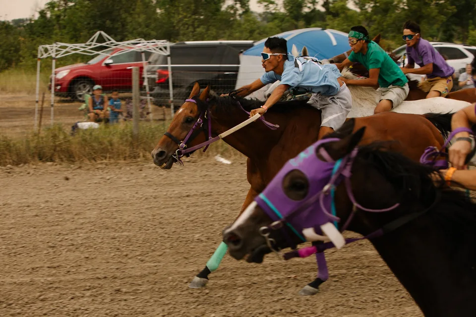 Riders in blue, green, and purple pass close together on the relay track.