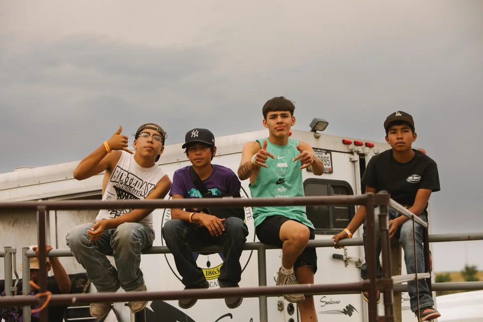Four spectators sit together on top of a metal fence.
