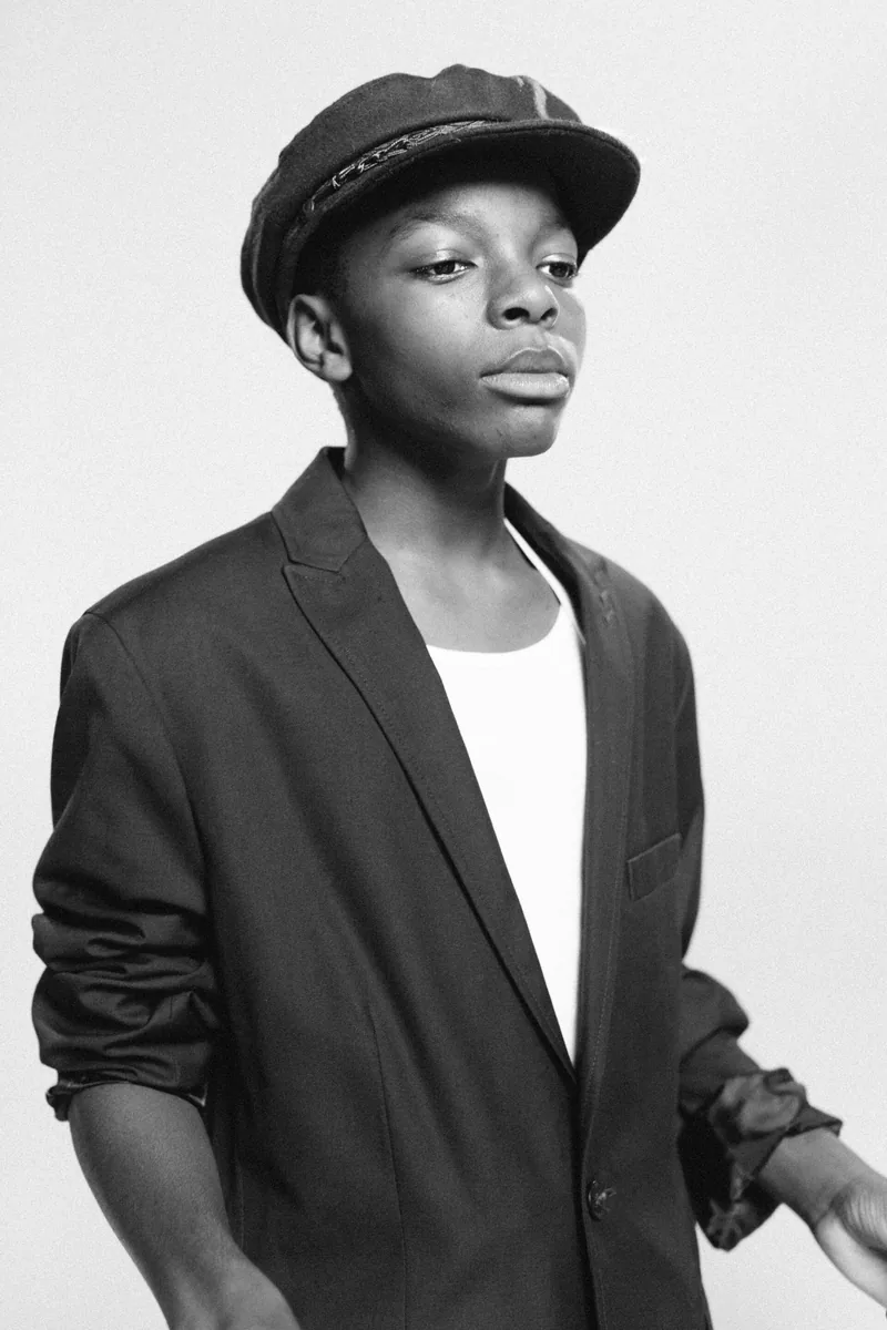 Black-and-white portrait of a child wearing a cap and dark blazer.