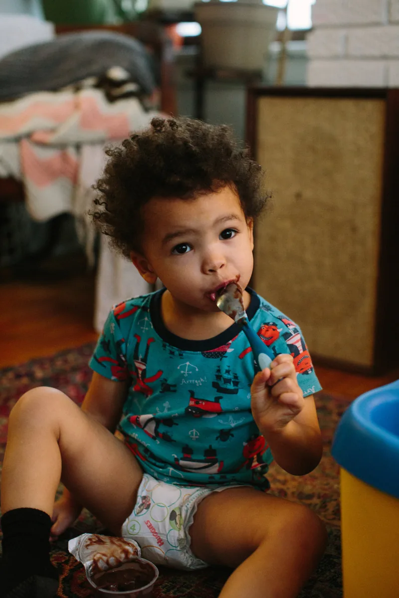 A small child eating while seated indoors in a colorful printed shirt.