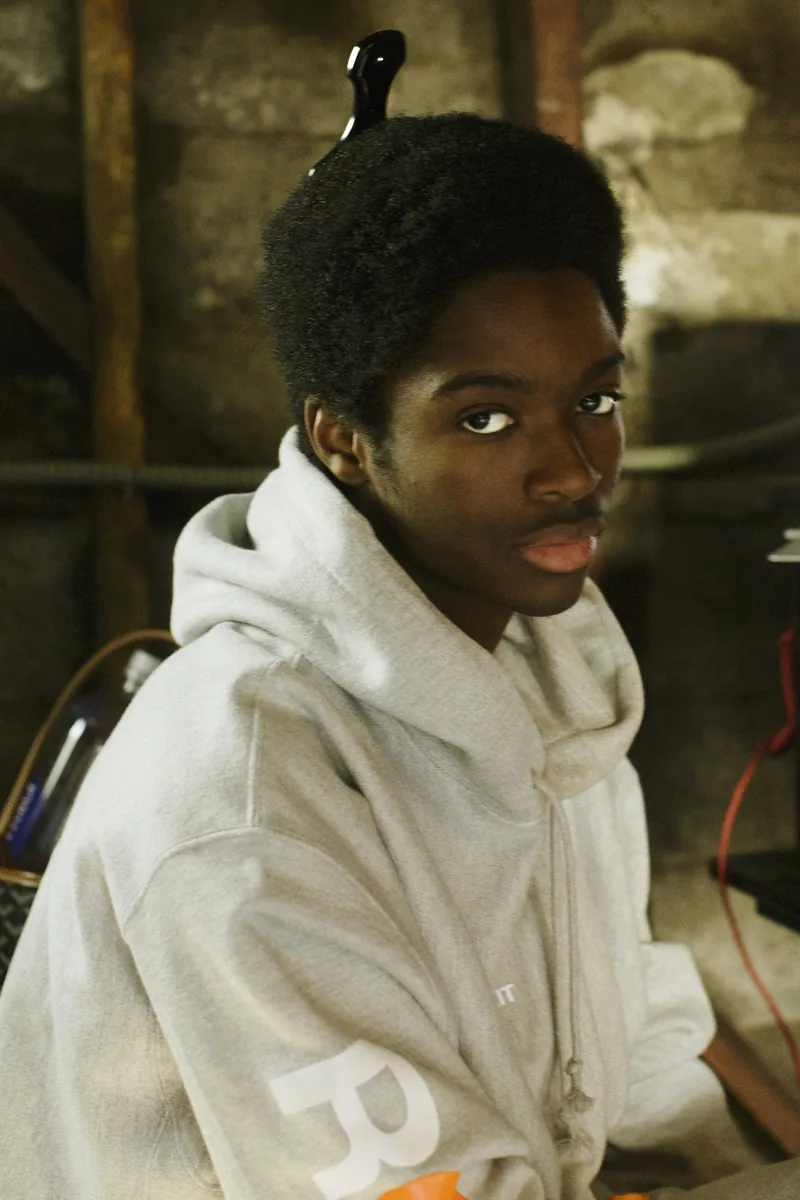 Portrait of a child in a light-colored hooded jacket sitting indoors.