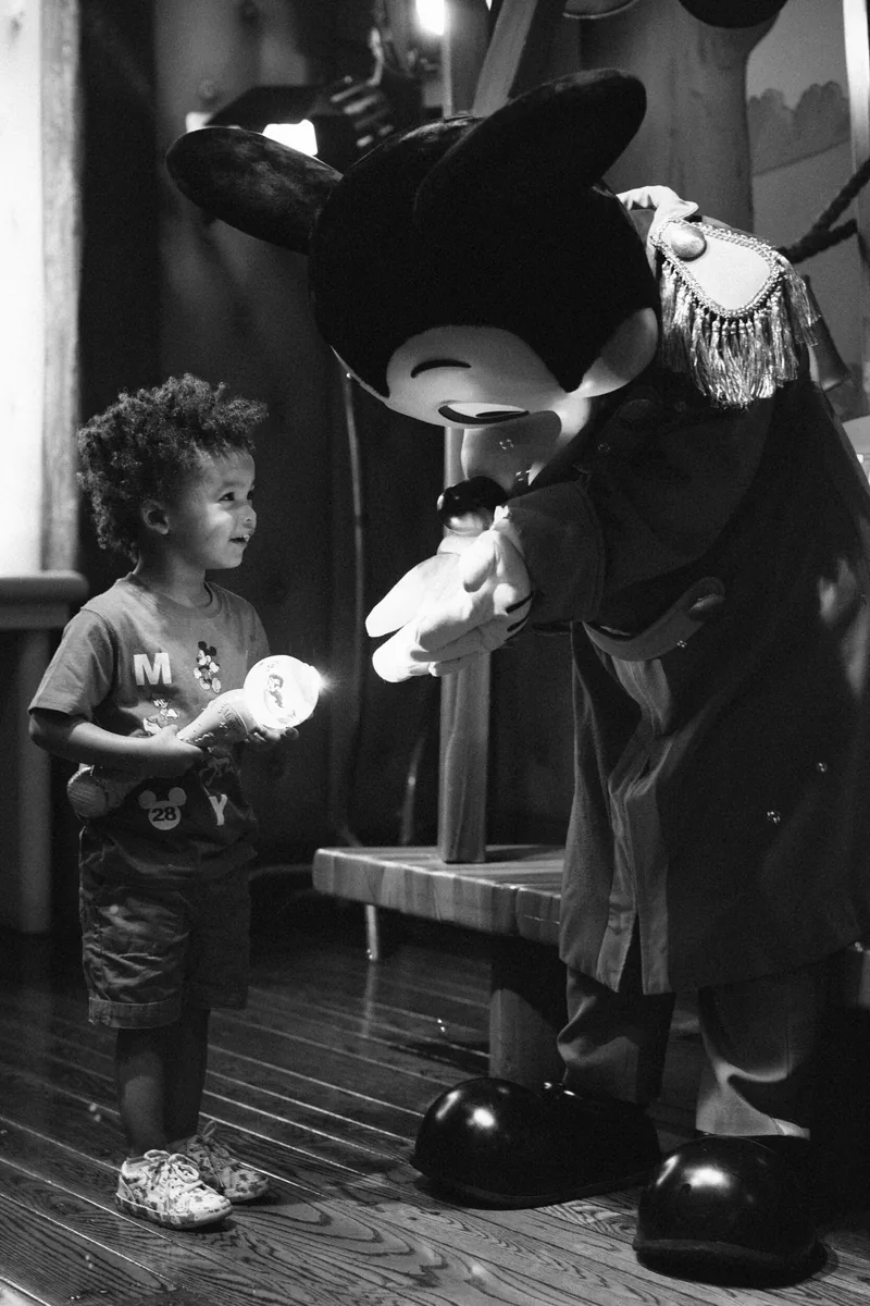 A small child meeting a person in a Mickey Mouse costume, photographed in black and white.