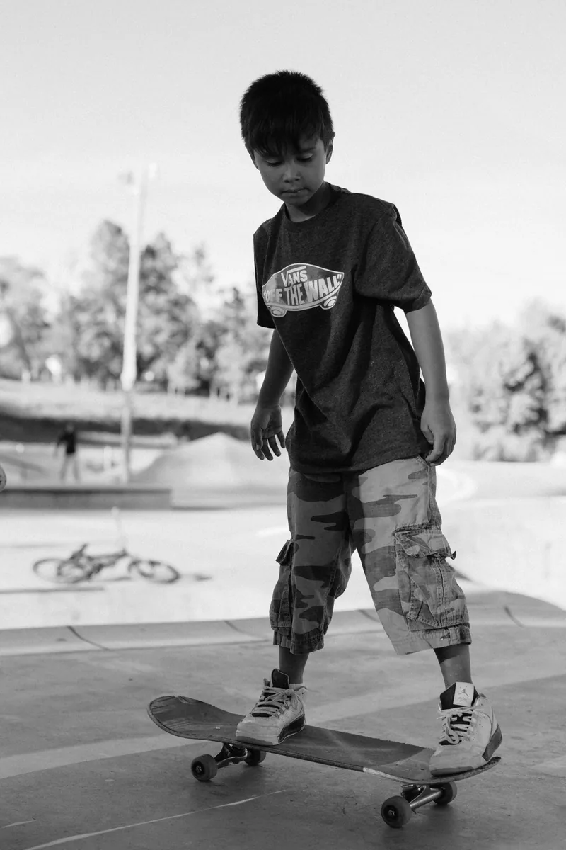 Black-and-white photograph of a child balancing on a skateboard at a skate park.