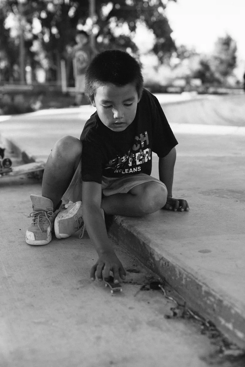 A child crouching beside a concrete ledge and playing with a small toy, in black and white.