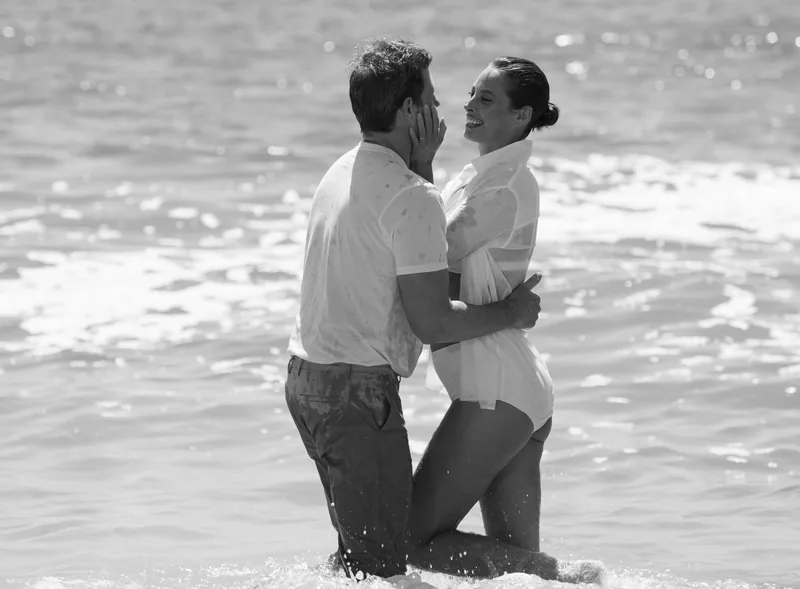 Black-and-white photograph of two models embracing in shallow ocean water.