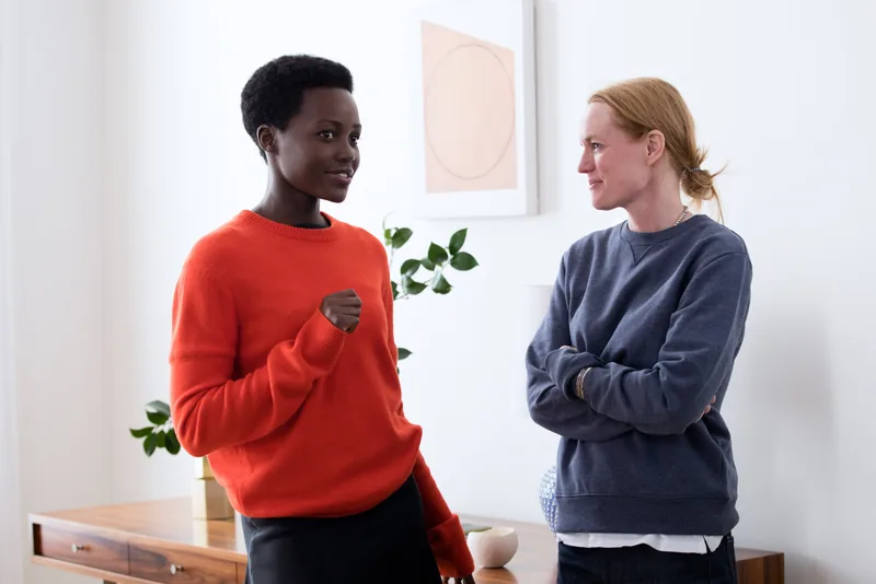 Two models in red and blue sweaters talking in a sunlit room.