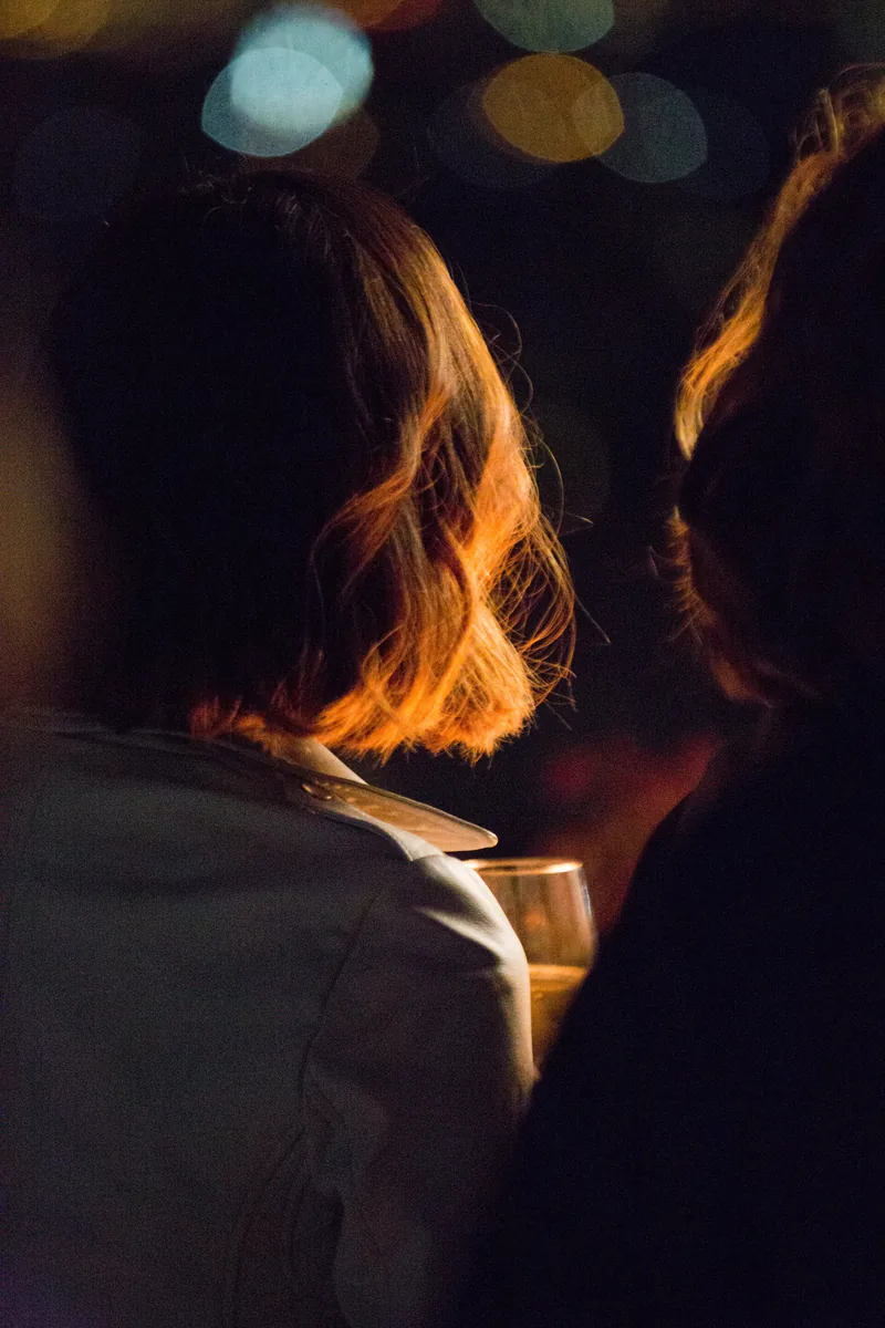 Evening portrait from behind, with warm light catching a woman's short hair and blurred lights in the background.