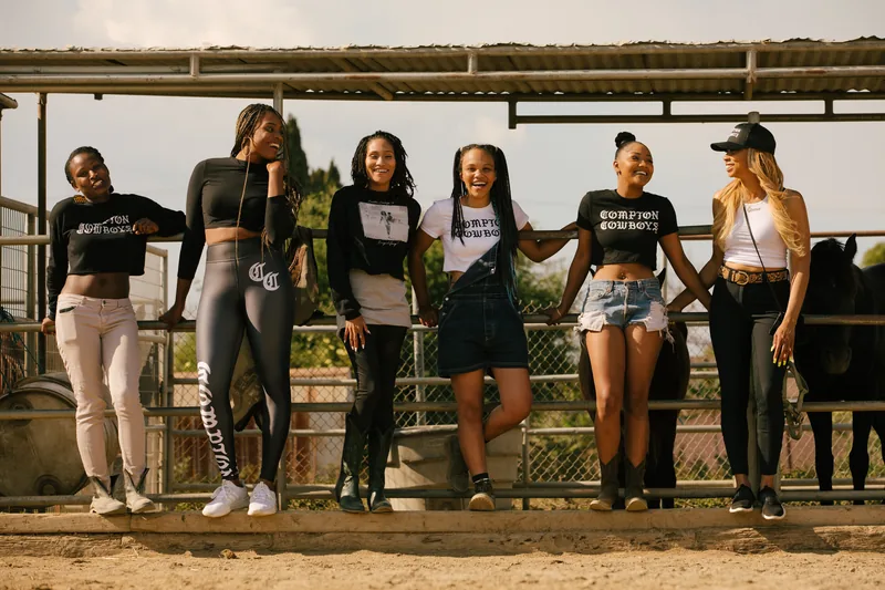Six women standing together beside a horse enclosure.