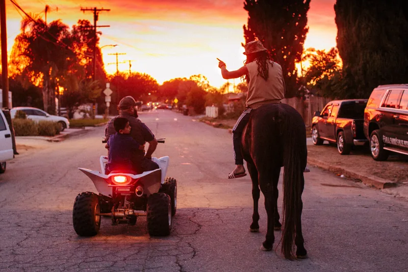 A horse rider and a person on an all-terrain vehicle traveling down a street at sunset.