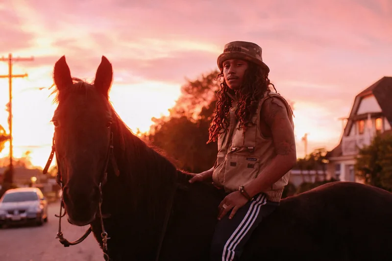 A rider on a horse beneath a vivid pink sunset sky.