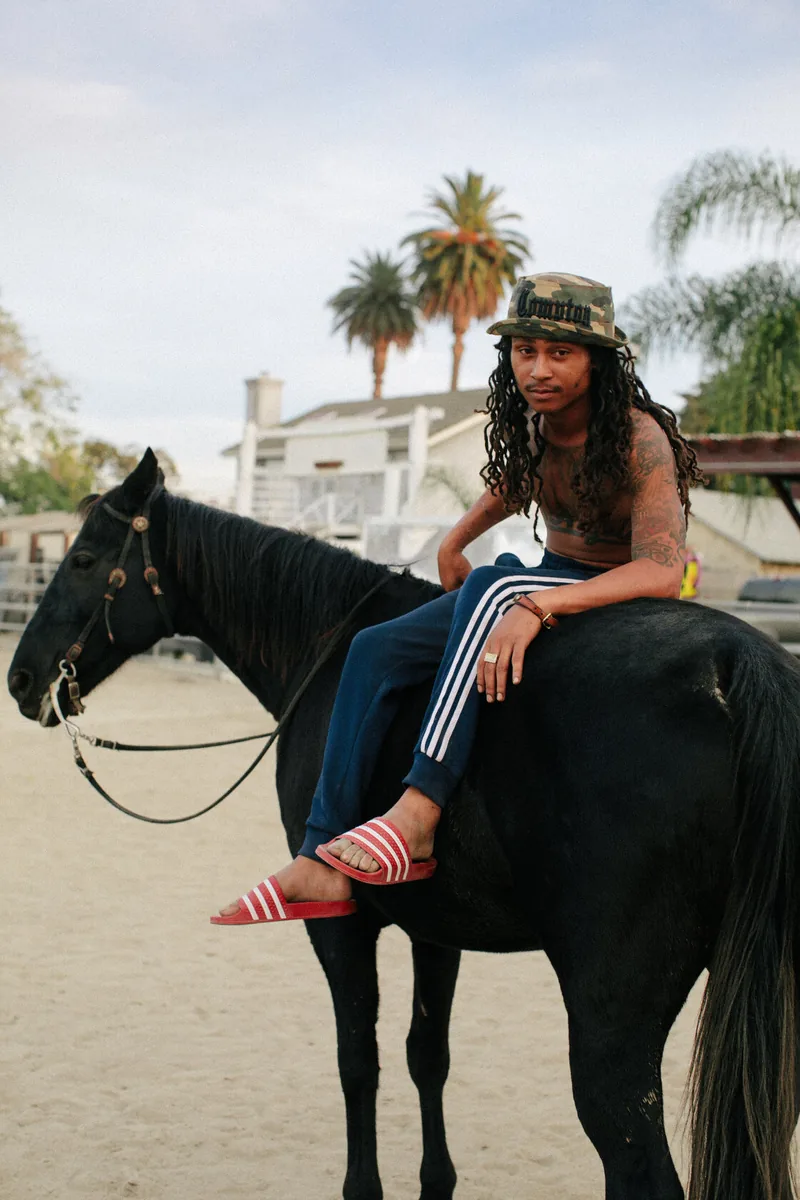 A rider wearing striped trousers and red sandals sitting on a dark horse.