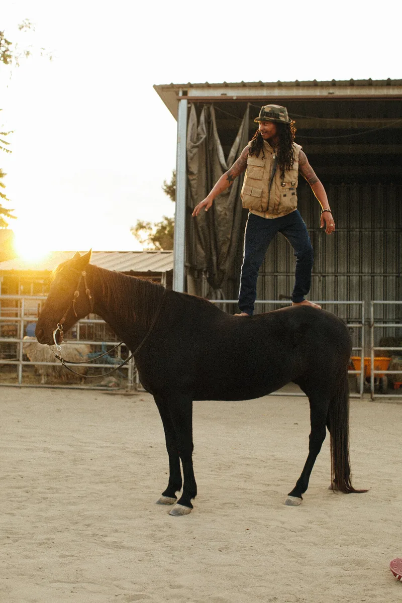 A person standing upright on a horse's back in an outdoor enclosure.
