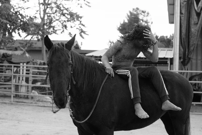 Black-and-white photograph of a barefoot rider leaning forward on a horse.
