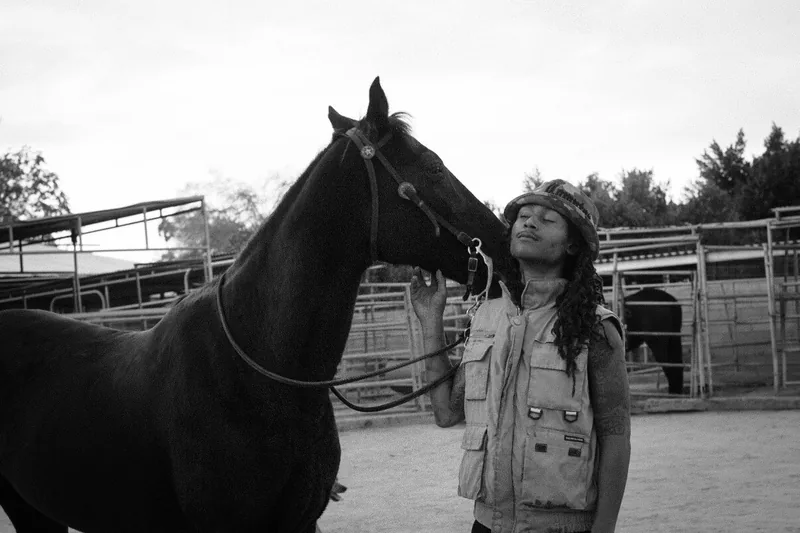 A person looking up at a horse's face in a paddock, photographed in black and white.