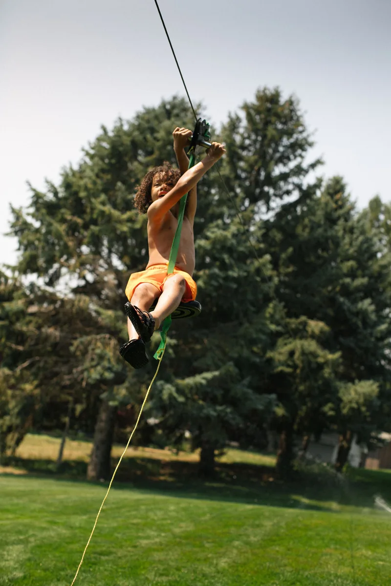 A child riding a zip line above a grassy lawn.