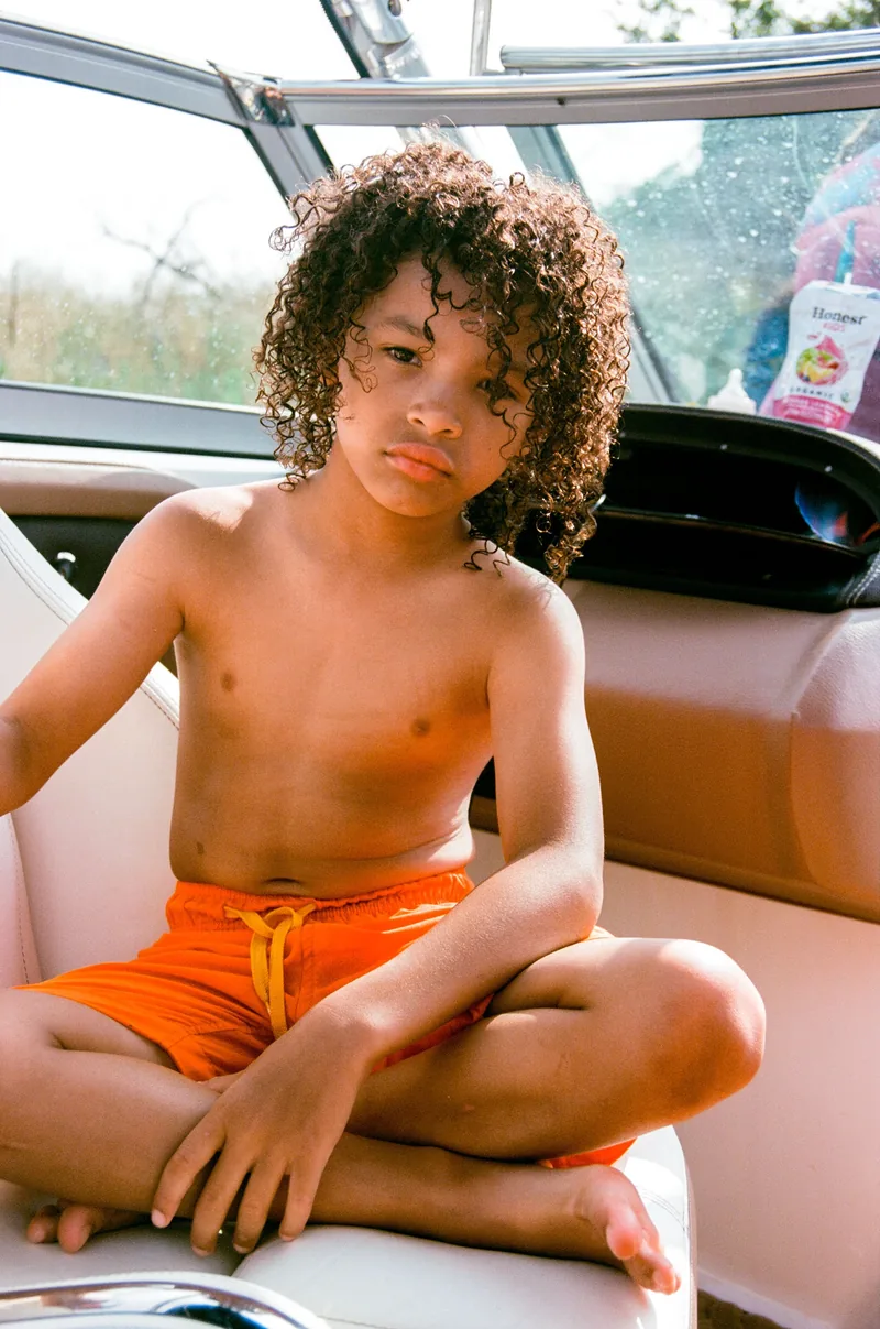 A child in orange shorts sitting cross-legged on a boat seat.