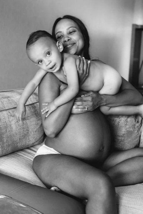 Black-and-white portrait of a seated woman smiling while holding a child across her shoulders.