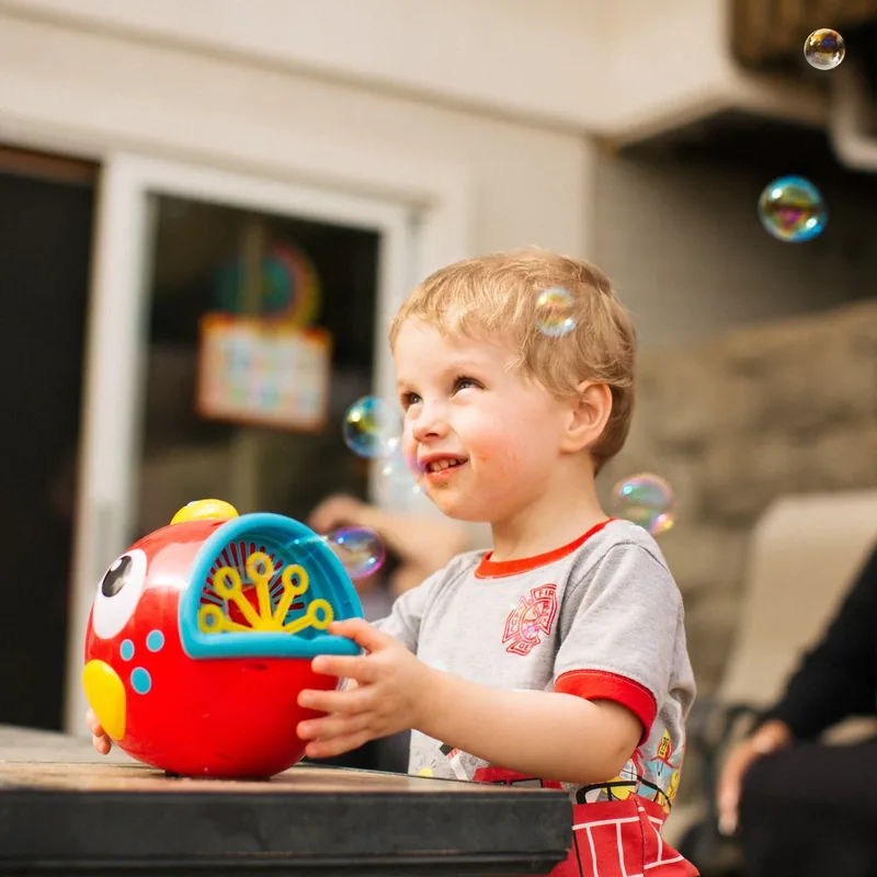 A smiling child playing with a colorful bubble machine outdoors.