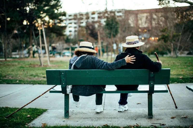 Two people in hats sitting close together on a park bench, seen from behind.