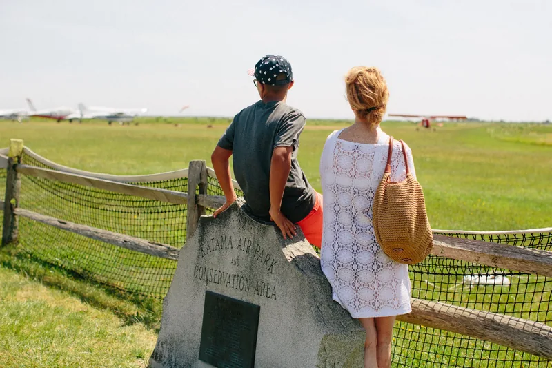 Two people leaning against a fence overlooking a green field.