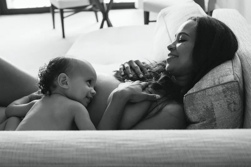 Black-and-white photograph of a woman reclining on a sofa with a child resting beside her.