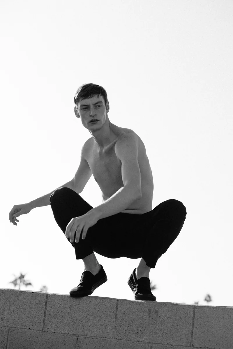 Black-and-white photograph of a model crouching on a low wall.