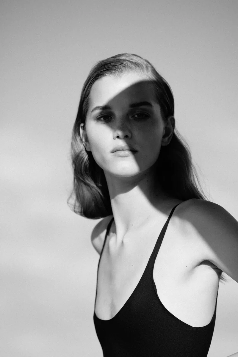 Black-and-white portrait of a model with short hair and a black camisole, her face partly in shadow.