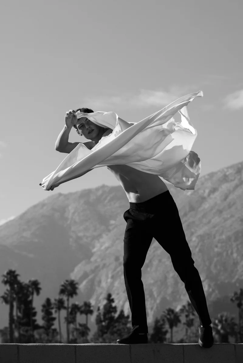 A model sweeping white fabric overhead against mountains in black and white.