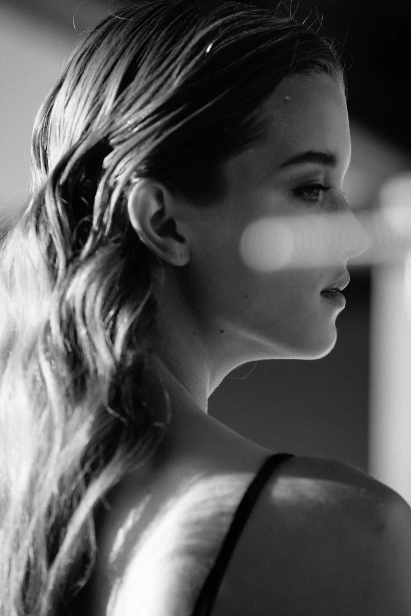 Black-and-white profile portrait of a model with slicked-back hair and a band of light across her face.