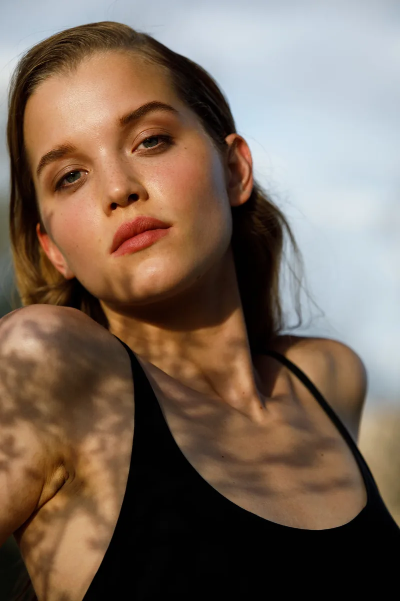 Portrait of a model in a black camisole with leaf shadows across her skin.