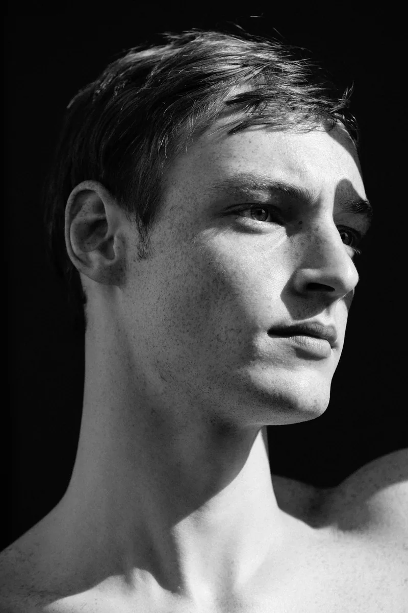Black-and-white close-up of a model looking to the side in strong sunlight.