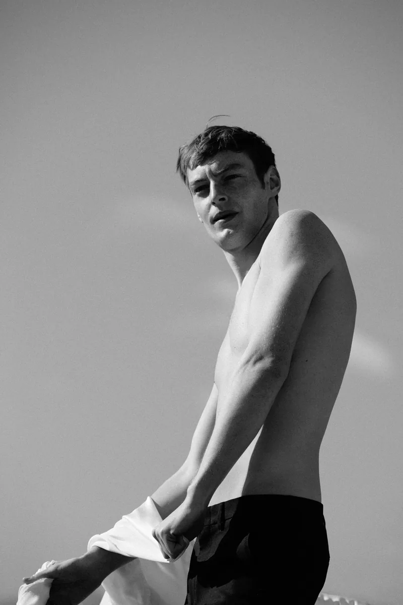 Black-and-white portrait of a model holding white fabric at his waist.