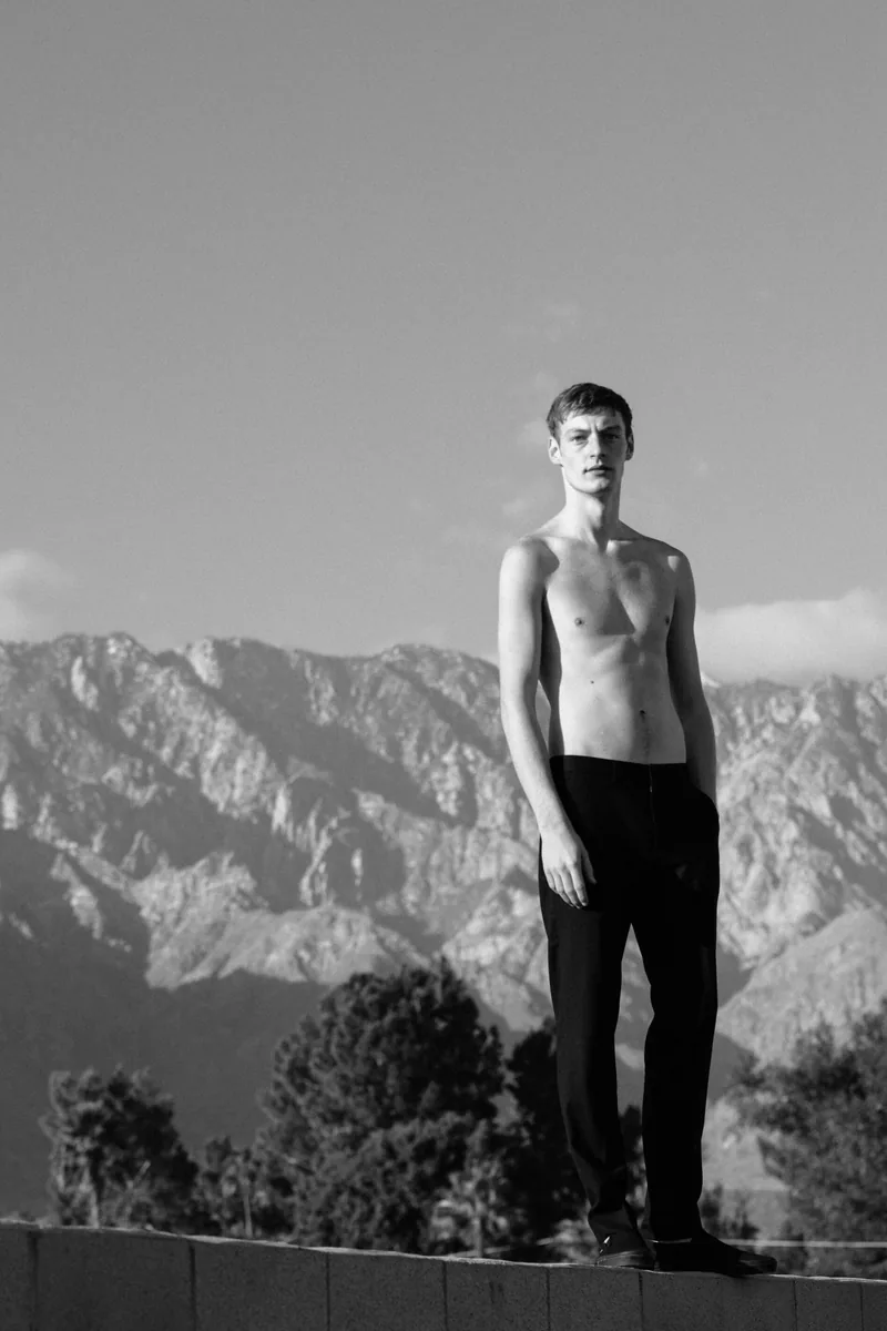 A model standing before a rugged mountain range in black and white.