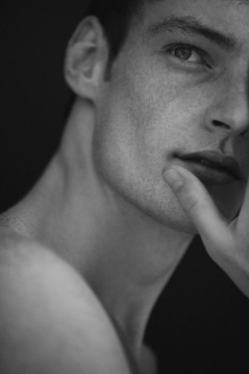 Black-and-white close-up of a model resting a finger against his chin.