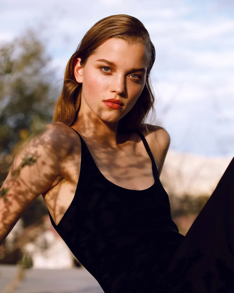 Portrait of a model in a black top under dappled sunlight.