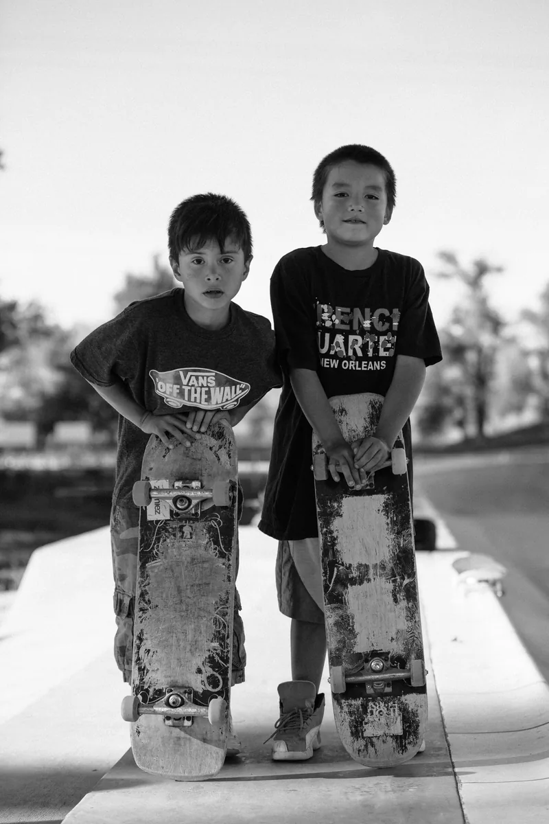 Two children holding upright skateboards beside each other, in black and white.