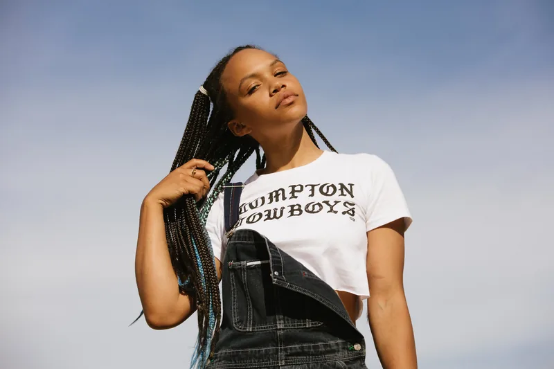 A woman wearing a Compton Cowboys shirt with her face tilted toward the sun.