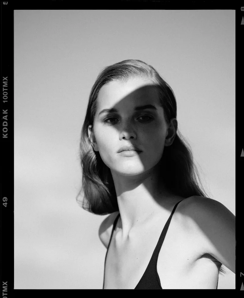 Black-and-white portrait of a model in a black camisole, framed by a photographic negative border.