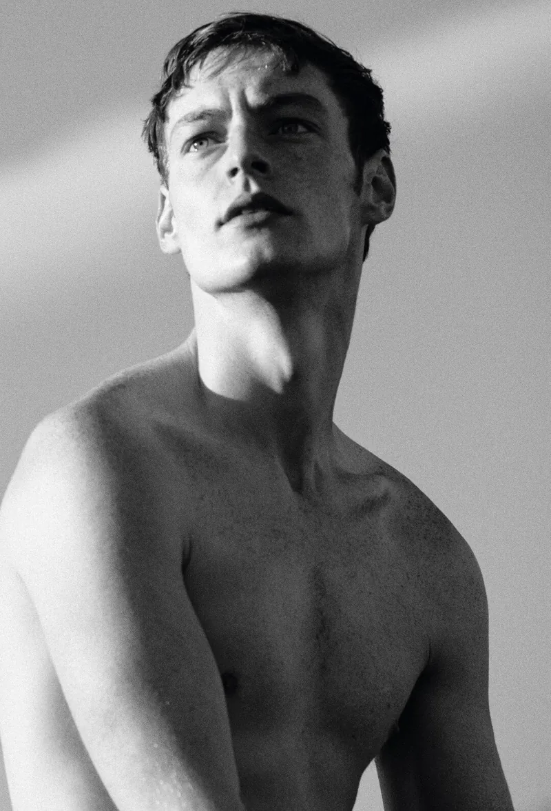 Black-and-white portrait of a model looking upward with sunlight across his face.